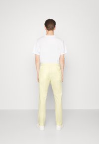 Ljust gula byxor med elastisk midja och en slät textur, i kombination med en enkel vit t-shirt med kort ärm och vita sneakers.