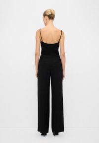 Crop top noir côtelé avec fines bretelles associé à un pantalon large noir comportant un détail de design sur le côté et une texture lisse.