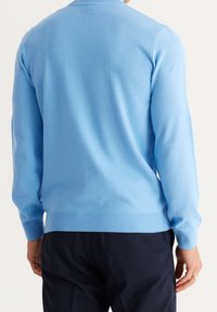 Ljusblå, stickad tröja med rundad hals och långa ärmar, med ribbade mudd och nederkant. Slät textur, bakvy visas.