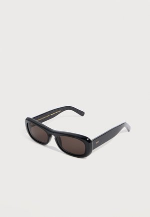 Black rectangular sunglasses with dark lenses and thick frames angled on a white surface, featuring small gold lettering on temple arms.