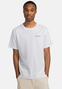 Camiseta de algodón blanca con cuello redondo, que presenta un pequeño logo marrón de "Element" en el lado izquierdo del pecho. Ajuste clásico y mangas cortas.
