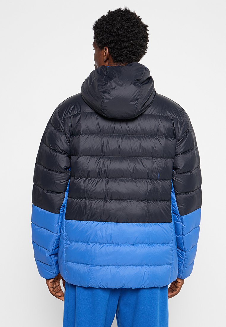 Doudoune avec capuche, présentant une partie supérieure noire et une partie inférieure bleue. Elle a des panneaux matelassés et une texture lisse et brillante.