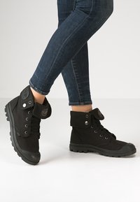 Bottines en toile noires avec une semelle en caoutchouc, bout rond et laçage par œillets. Elles présentent un revers plié et un logo sur le côté.