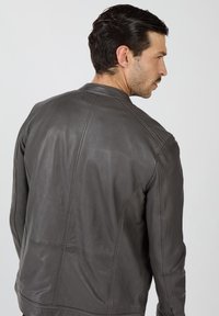 Szara skórzana kurtka o gładkiej fakturze, z pikowanymi detalami na ramionach i minimalistycznym designem. Widok z tyłu ukazuje przeszycia.