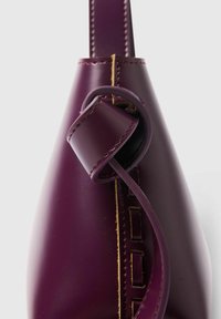 Djup lila läderväska med en slät yta, med en snoddrem och kontrasterande söm längs en utskärning.