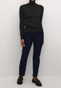 Ciemnoszary sweter z golfem, dopasowany krój z długimi rękawami, w połączeniu z ciemnoniebieskimi dżinsami. Czarne mokasyny z detalem z klamrą.