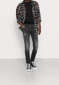 Černá a oranžová kostkovaná flanelová košile přes černé tričko, doplněná o roztrhané tmavé džíny a černé tenisky s vysokým střihem.