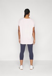 Světle růžové oversized tričko s krátkými ohrnutými rukávy, kombinované s námořnickými legínami do tří čtvrtin a bílými sportovními botami, zobrazené ze zadní strany.