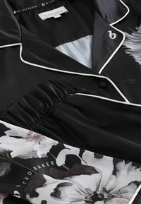 Set de pijama din satin negru, cu accente florale și detalii cu pieptăn alb. Talie elastică pentru confort. Eticheta brandului vizibilă la guler.