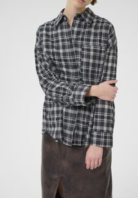 Person wearing a black and white plaid button-up shirt with a chest pocket and a dark brown leather skirt with front slit.