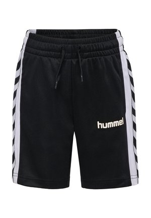 Dreng med krøllet hår iført sort mønstret T-shirt og sorte sportsshorts med hvide chevronstriber, der kigger ned på sine shorts.