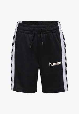 Dreng med krøllet hår iført sort mønstret T-shirt og sorte sportsshorts med hvide chevronstriber, der kigger ned på sine shorts.