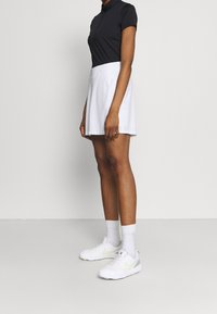 Czarna koszulka polo z krótkim rękawem połączona z białą sportową spódniczką typu skort. Białe tenisówki z jasnoszarymi i neonowozielonymi akcentami dopełniają strój.