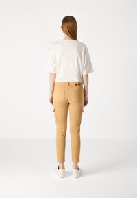 Beige cargobroek met taperende pijpen, zijzakken en een eenvoudig ontwerp van riemlussen, gecombineerd met een witte short-sleeve top.