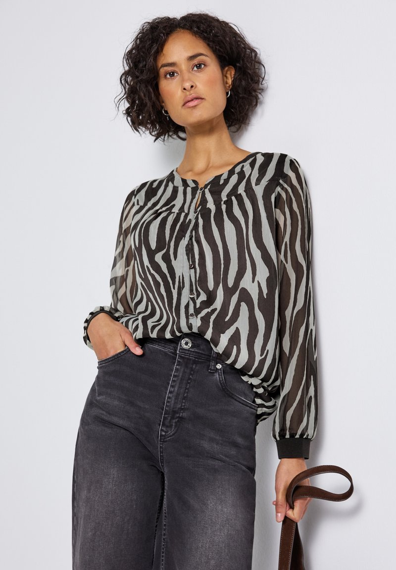 Blusa con stampa zebra nera e grigia, con abbottonatura frontale, maniche lunghe a palloncino e vestibilità ampia, abbinata a jeans scuri a vita alta.