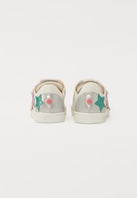 Hvite sneakers med sølvfargede, glitrende accenter og fargerike stjerneapplikasjoner på sidene. Gummisåler og teksturerte stoffdetaljer.