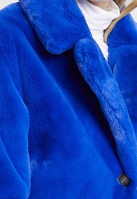 Faux fur-kappa i levande blått med en bred krage, som har en mjuk textur och en synlig knappstängning.