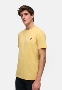 Geel katoenen T-shirt met korte mouwen, ronde hals en zwart logo-opnaad op de linkerkant van de borst. Soepele textuur, normale pasvorm en eenvoudig ontwerp.