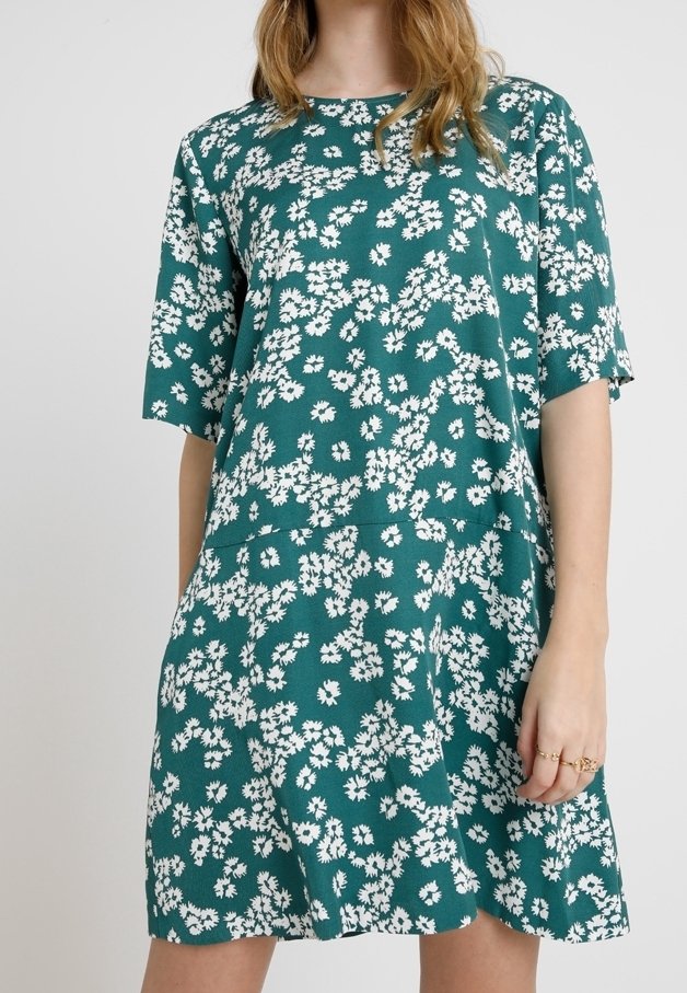 Vestido verde azulado hecho de una tela suave con un corte holgado, que presenta un patrón floral blanco. Mangas cortas y un escote redondo.