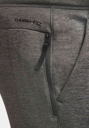 Nahaufnahme von grauer Stoffhose mit einer vertikalen schwarzen Reißverschlusstasche und "THERMAL-FITT" über der Tasche gestickt.