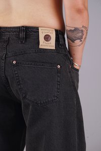 Black denim jeans with a leather patch on the waistband, featuring copper accents on the back pockets and a relaxed fit.