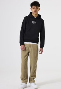 Sudadera negra con capucha y texto blanco, combinada con pantalones de pana color marrón claro y zapatillas blancas. Diseño sencillo sin patrones.