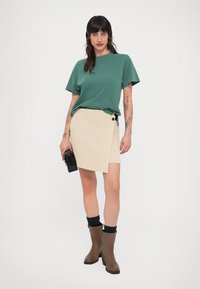 Πράσινο κοντομάνικο μπλουζάκι συνδυασμένο με μπεζ φούστα τύπου φάκελος με λεπτομέρεια κουμπιού. Καφέ μπότες μέχρι τον αστράγαλο και μια μικρή μαύρη τσάντα ολοκληρώνουν την εμφάνιση.