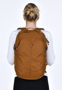 Zaino in tessuto marrone con più scomparti, spallacci regolabili e chiusure a zip. Texture liscia e design minimale.