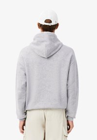 Felpa con cappuccio grigio chiaro caratterizzata da un motivo floreale strutturato, con tasca a marsupio e polsini a costine. Indossata con pantaloni cargo beige.
