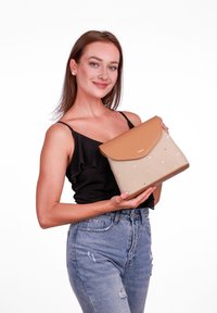 Tělová a béžová kabelka s klopovým uzávěrem, zdobená tečkovaným vzorem a pevným designem. Vyrobena z texturovaných materiálů, držena osobou.