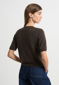 Brązowy sweter z krótkim rękawem o miękkiej teksturze. Posiada okrągły dekolt i dopasowany fason. Nosi się go z ciemnoniebieskimi dżinsami o szerokich nogawkach.