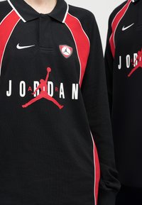 Μακρυμάνικα αθλητικά φανελάκια Jordan σε μαύρο και κόκκινο χρώμα, με λευκά λογότυπα Nike και κόκκινο σιλουέτα Jumpman στο κέντρο του στήθους.