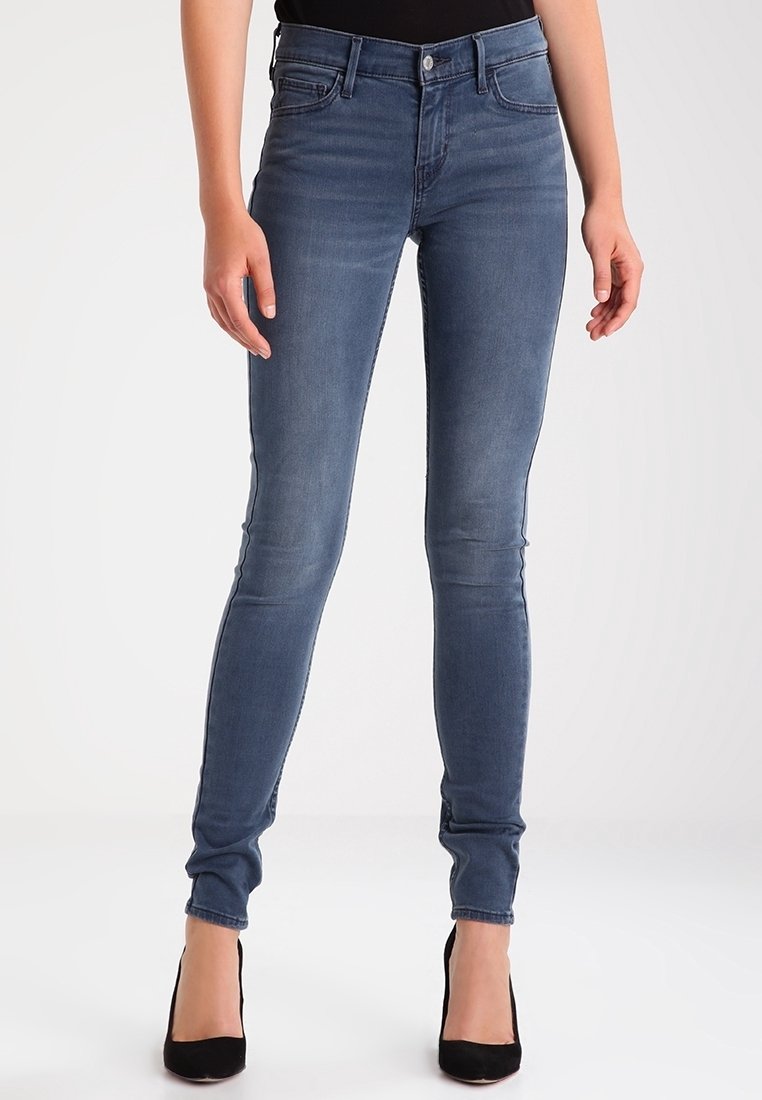 Jean skinny en denim bleu moyen avec un effet délavé, doté de cinq poches, d'une braguette à boutons à l'avant et d'une coupe ajustée le long de la jambe.