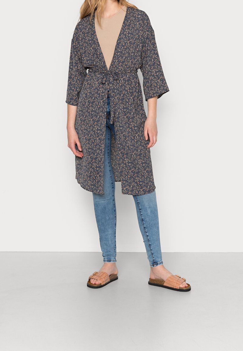 Dunkelgrauer Kimono mit Blumendruck, einem gebundenen Taillengürtel, 3/4-Ärmeln und einem lockeren Schnitt, kombiniert mit hellblauen Skinny Jeans und hellbraunen Sandalen.