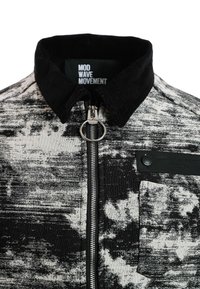 Chaqueta de patrón en blanco y negro que presenta un cuello de pana, cremallera plateada y un bolsillo en el pecho con detalle de botón.