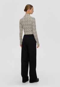 Dopasowana bluzka z długim rękawem w czarno-beżowy druk w cętki, połączona z czarnymi spodniami o szerokich nogawkach z wysokim stanem. Gładka tekstura materiału.