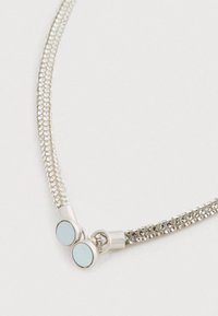 Hopeaketjun hopeanvärinen ketju, jossa on upotettuja kiteitä ja pyöreä magneettikappale, valkoisella taustalla.