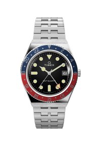 Reloj de cuarzo Timex GMT con esfera negra, caja y pulsera de acero inoxidable plateado, bisel giratorio rojo y azul, y marcadores lumínicos blancos.