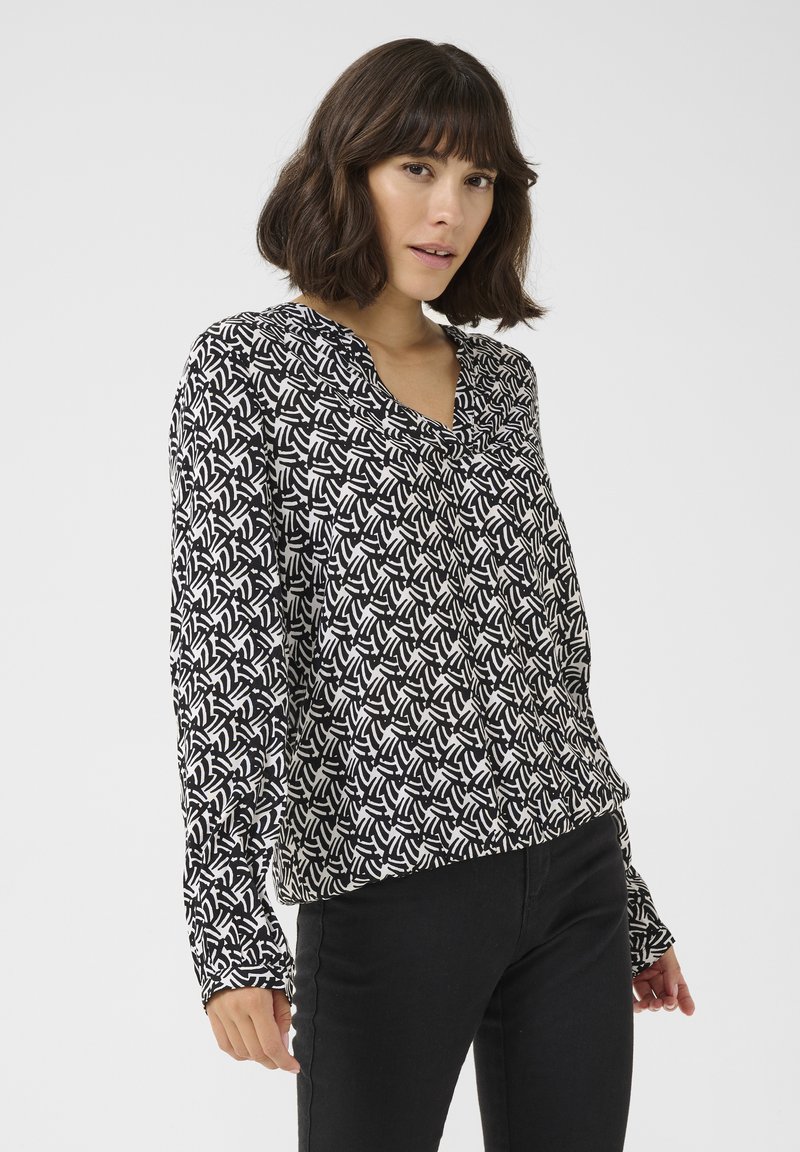 Black and white long-sleeve blouse with a geometric pattern, featuring a V-neckline and soft, lightweight fabric. Seam detailing visible.