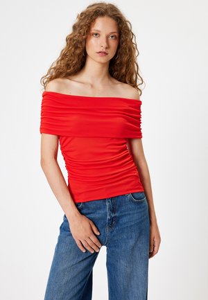 Top rojo de un solo hombro con textura fruncida, silueta ajustada y material suave. Combinado con vaqueros azules de cintura alta.