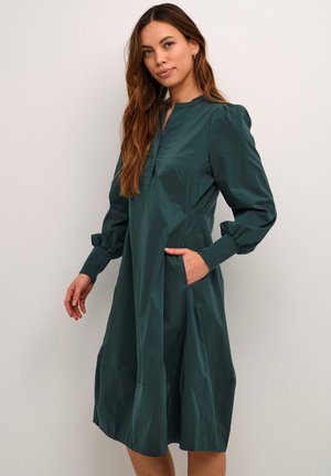 Teal dress in lightweight fabric, featuring long puff sleeves, a mock neck, and side pockets with a tiered hem detail.
