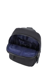 Borsa compatta nera con chiusura a zip, dotata di fodera interna blu navy e patch con logo. I materiali includono tessuto testurizzato e dettagli in pelle.