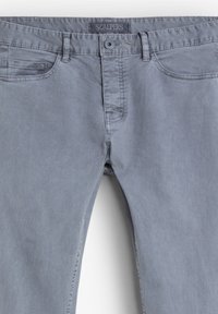 Pantalones de algodón gris con un corte recto, que cuentan con una cremallera en la bragueta, cuatro bolsillos y una etiqueta de marca en la cinturilla. Textura suave y diseño minimalista.