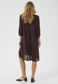 Abito tiered color bordeaux con maniche a tre quarti, in tessuto leggero e vestibilità comoda. Abbinato a scarpe lucide di un bordeaux scuro.