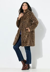 Leopardprint faux fur frakke med krave, frontknaplukning og sidelommer; stylet med mørke denimjeans og brune ankelstøvler.