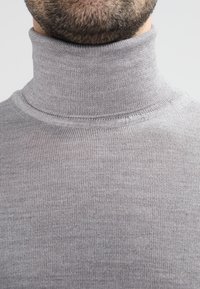 Pull à col roulé gris avec une coupe ajustée, une texture côtelée et un col montant, vue en gros plan mettant en valeur les détails du tissu et les coutures.