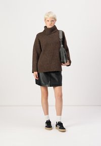 Un pull col roulé en tricot marron associé à une jupe en cuir noire, des chaussettes blanches et des baskets noires avec un sac gris. Texture lisse et coupe décontractée.