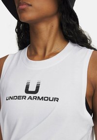 Bílý bezramínkový top z bavlny, s černým logem "U" a textem "UNDER ARMOUR". Zaoblený výstřih a čisté detaily šití.