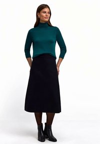 Türkisfarbener Rollkragenpullover kombiniert mit einem schwarzen Midirock, glatter Textur, schmaler Passform und schwarzen Stiefeletten bis zum Knöchel.