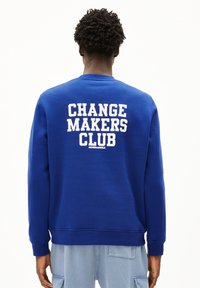 Blauw sweatshirt met een ronde halslijn, voorzien van witte blokletters "CHANGE MAKERS CLUB" op de achterkant. Zacht materiaal, ontspannen pasvorm, geribbelde mouwen.